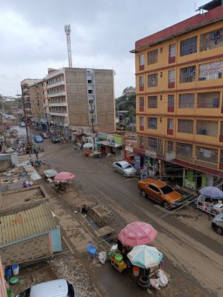 Photo of a street with street vendors, some multi-storey residential buildings, and some cars