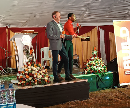 two men with microphones on a conference stage in a large tent