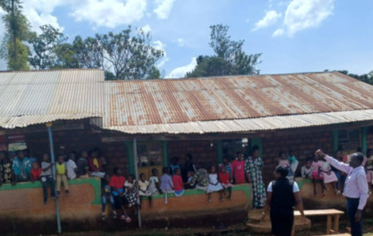 People including many children in front of a long low building