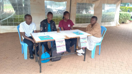 A table with “compassion week” posters and four young people sitting behind it.