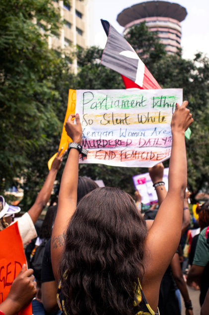 People demonstrating; a woman is holding up a placard which reads
     “Parliament Why So Silent While Kenyan Women Are MURDERED DAILY?? # END FEMICIDE!!”